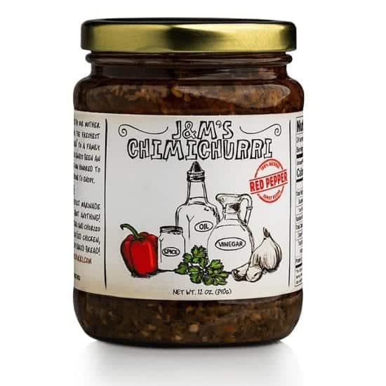 This is a jar of J&M's Chimichurri labeled as "Red Pepper." The packaging showcases an artisanal aesthetic, characterized by hand-drawn illustrations of its core ingredients, including oil, vinegar, spice, garlic, and notably, a red pepper which differentiates this variant from the original. The red "Red Pepper" badge on the label suggests that this particular version of the chimichurri sauce offers a mild sweet taste, enhancing its flavor profile. The label confirms that the net weight of the product is 12 oz (340g). The design consistently emphasizes a sense of authenticity and tradition, with the richly textured contents promising a robust and zesty experience. The added illustration of the red pepper hints at a sweeter, perhaps more adventurous take on the classic chimichurri sauce.