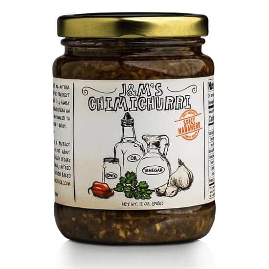 This jar features J&M's Chimichurri labeled with a "Spicy Habanero" badge. The design showcases a handcrafted appeal, highlighted by hand-drawn illustrations of the main ingredients like oil, vinegar, spice, garlic, and notably, a habanero pepper, indicating the spicy character of this variant. The badge, in bright red with the label "Spicy Habanero," signals that this edition of chimichurri sauce promises an intense heat, ideal for those who appreciate a fiery kick in their dishes. The product has a net weight of 12 oz (340g). Like the other versions, the design underscores an authentic and traditional feel, suggesting that the sauce is crafted with care. The inclusion of the habanero pepper illustration hints at an elevated level of spiciness for those seeking a bolder flavor experience.