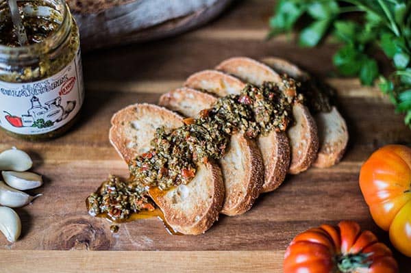 Toasted slices of bread generously topped with rich and flavorful chimichurri sauce, with a hint of the sauce jar in the background.