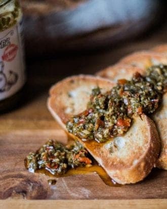 Toasted slices of bread generously topped with rich and flavorful chimichurri sauce, with a hint of the sauce jar in the background.
